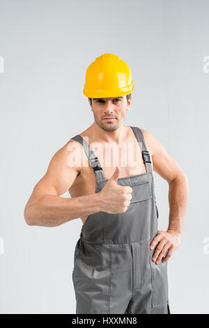 Handsome professional male builder showing thumb up on grey Stock Photo
