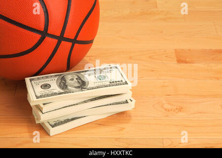 Basketball and stack of one hundred dollar bills on wooden court floor