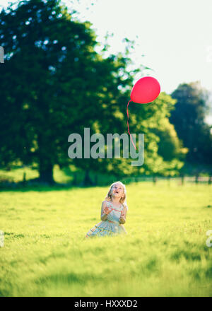 Blond girl letting go of a single red balloon in the Countryside Stock Photo