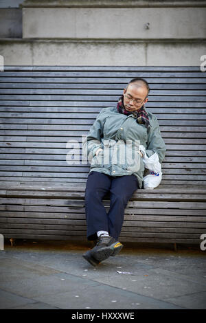 Asian man sleeping on a public seating bench near Peter Square, Manchester city centre,  England, UK. Stock Photo