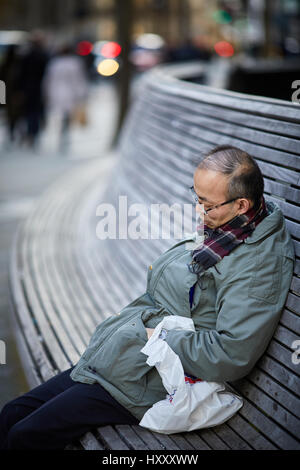 Asian man sleeping on a public seating bench near Peter Square, Manchester city centre,  England, UK. Stock Photo