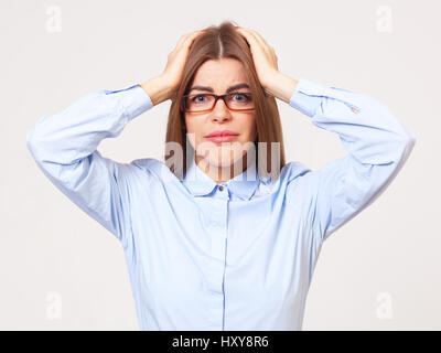 Studio portrait of upset young business woman standing in formal blue shirt on gray background. Stock Photo