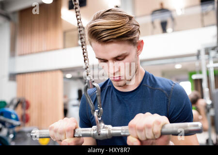 Young handsome fit man working out on pull-down machine in gym. Bodybuilder exercising with cable weight machine. Stock Photo
