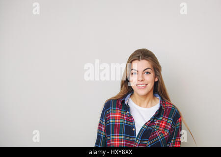 Studio portrait of happy young woman in plaid shirt posing against wall. Stock Photo