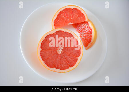 High angle view of a closeup of Pink grapefruit half and slices on a white plate and background Stock Photo