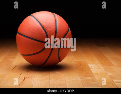 A basketball with a dark background on a hardwood gym floor Stock Photo
