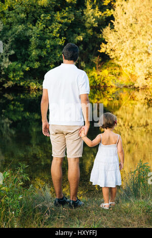 Father and daughter holding hands exploring the river in summer. Back view Stock Photo