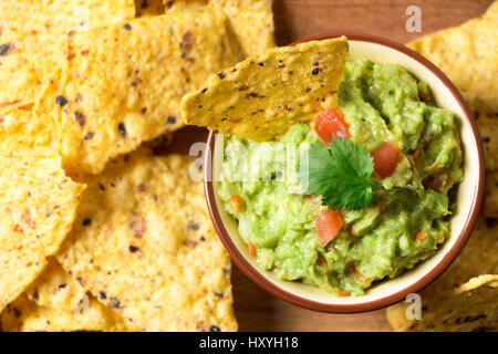 Guacamole bowl with tortilla chips on a wooden cutting board. Top view Stock Photo