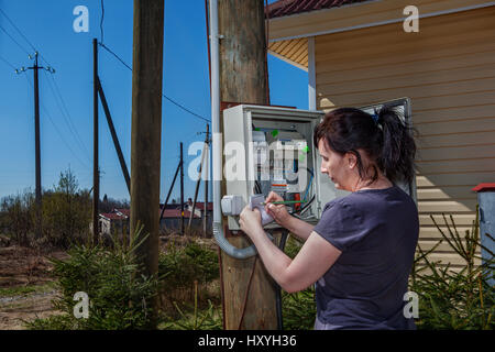 Peasant Woman looking electric meter data in switchgear mounted on a wooden pole near farm house in countryside. Stock Photo