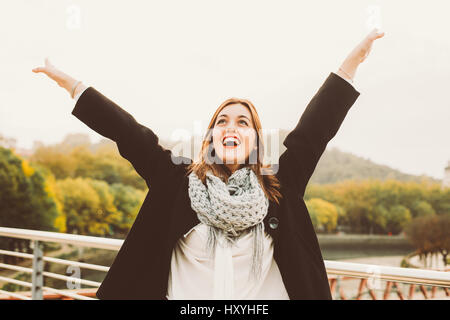 Happy young woman with arms raised celebrating something in the city Stock Photo