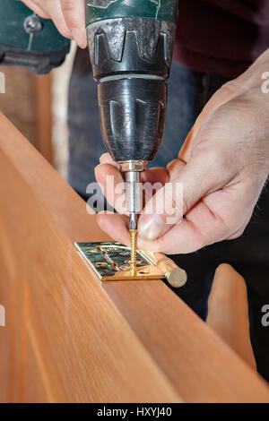Door installation, Close-up of cordless drill screwdriver in his hand carpenter, tightening screws for fastening brass hinges to a wooden interior doo Stock Photo