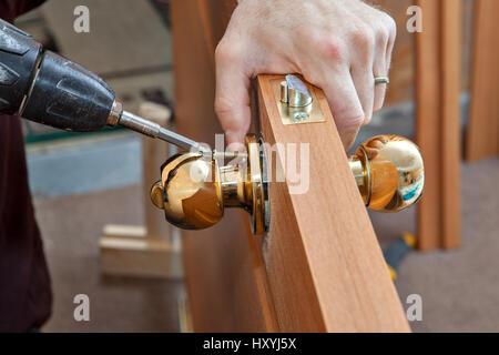 Install the door handle with a lock, Carpenter tighten the screw, using an electric drill screwdriver, close-up. Stock Photo