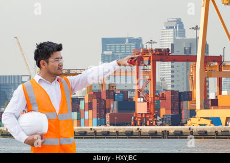 Port engineer standing in front of the industrial harbor with container cargo freight ship with working crane loading bridge in shipyard Stock Photo