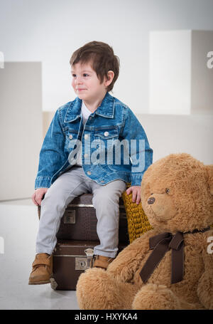 Little boy sitting on the travel retro brown suitcases in  jeans jacket with a bear Stock Photo