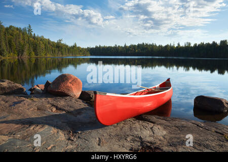 A yellow canoe rests on a rocky shore of a calm blue lake in the Boundary Waters of Minnesota Stock Photo
