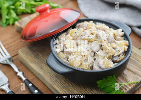 Fried mushrooms with sour cream in ceramic casserole on wooden background Stock Photo