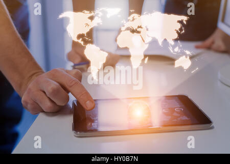 Global business concept with a world map hologram above a digital tablet and a team of two businessmen in background Stock Photo