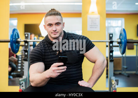 Young handsome man using phone while having exercise break in gym. Stock Photo