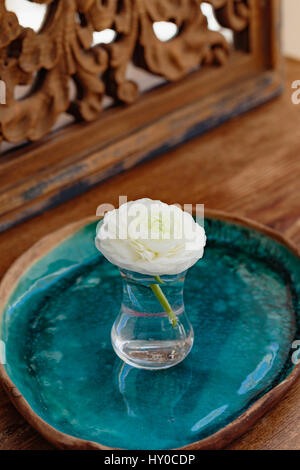 White ranunculus in glass of water placed on ceramic tray in front of mirrow decorated with carved wood Stock Photo