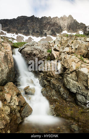 A rocky cliff looms overhead above this short but steep cascade of a small stream from melting snow in springtime Stock Photo