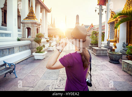 Tourist woman in the hat and purple t-shirt with photo camera in Wat Pho temple at sunset in Bangkok, Thailand Stock Photo