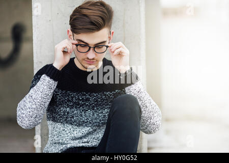 Fashionable man sitting near the wall with glasses on hands Stock Photo