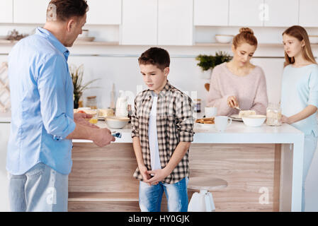 Dont do that any more. Caring angry father punishing his son and standing in the kitchen while mother and daughter eating breakfast Stock Photo