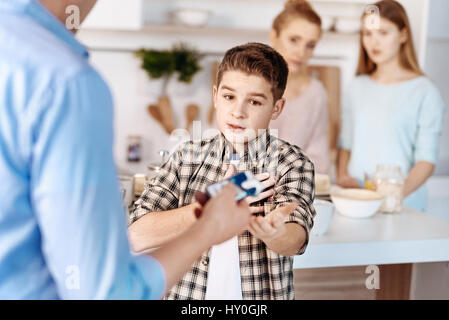 I swear. Little son looking at the pack of cigaretts and his father punishing him while standing in the kitchen Stock Photo