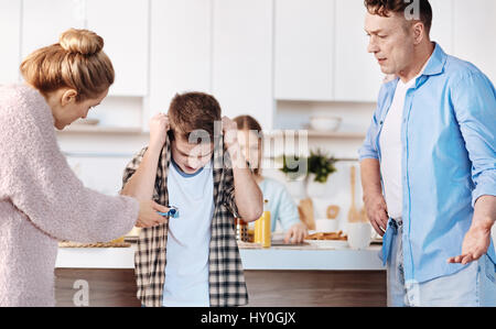 I dont believe you. Family couple standing in the kitchen and punishing their son for smoking Stock Photo