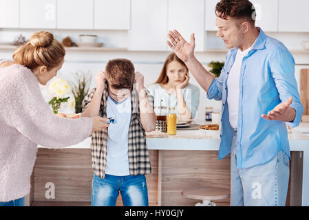 It is prohibited. Furious family couple holdign cigaretts and punishing their son while standing in the kitchen Stock Photo