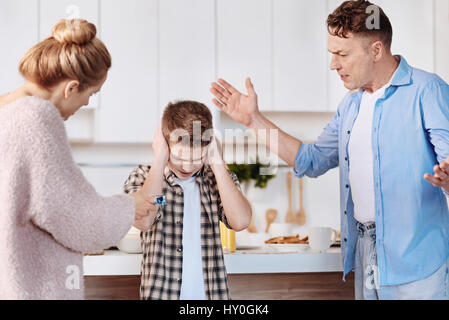 Bad behavior. Serious family couple scolding their son and warning him while standing in the kitchen Stock Photo