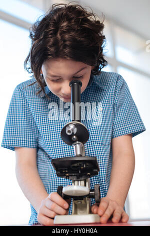Looking for something peculiar. Focused observant passionate boy being precise using a microscope for studying some kind of bacteria in a lab Stock Photo