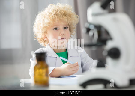 Schoolboy in white lab coat taking notes during scientific experiment Stock Photo