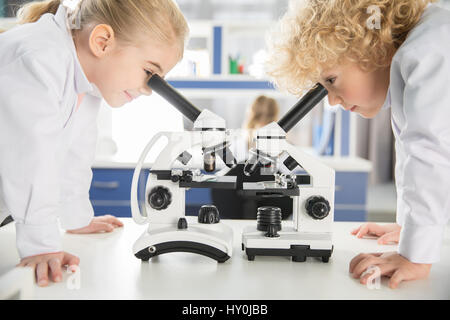 Schoolchildren in lab coats using microscopes in chemical laboratory Stock Photo