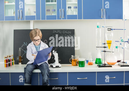 Little boy wearing lab coat making notes in clipboard in science laboratory Stock Photo