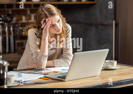 Upset young woman freelancer using laptop and thoughtfully looking away Stock Photo