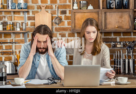 Upset young couple of freelancers working with papers and laptop in kitchen Stock Photo