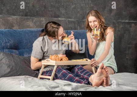 Young happy couple has breakfast in bed and drinks orange juice Stock Photo