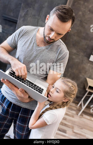 Father and cute little daughter standing and using laptop Stock Photo