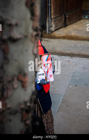 photo of David Bowie as Ziggy Stardust, cover of The Big Issue, peeking out from behind tree trunk, Stock Photo