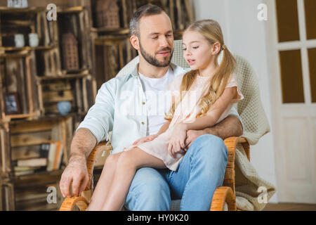 Smiling father and daughter sitting together in rocking chair Stock Photo