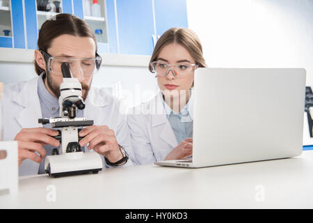 Two young scientists working in laboratory using microscope and laptop Stock Photo