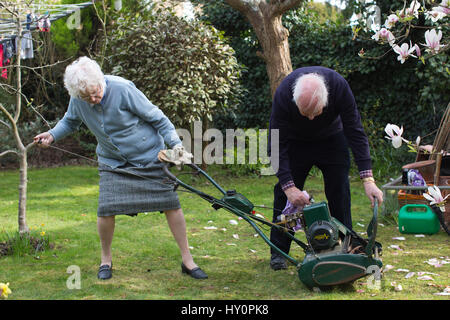 Elderly pensioners trying to start a petrol lawn mower in a English residential garden on a Spring afternoon, Surrey, England, United Kingdom Stock Photo