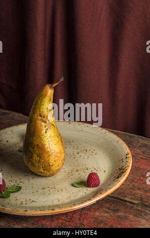 Isolated yellow pear on the plate with raspberries and mint on brown background Stock Photo