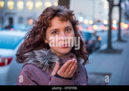 Portrait of young brunette woman blowing a kiss with windy hair Stock Photo