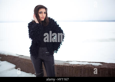 Armenian girl in a fur coat and leather legency is on the background of snow. Day. Stock Photo