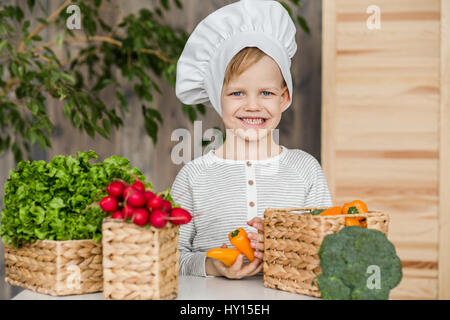 Cute boy in chef uniform with vegetables. Cooking in kitchen at home. Vegetarian. Healthy food Stock Photo