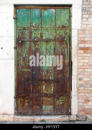 Old wooden green door with peeling paint and rusting hinges in an ancient brick wall Stock Photo