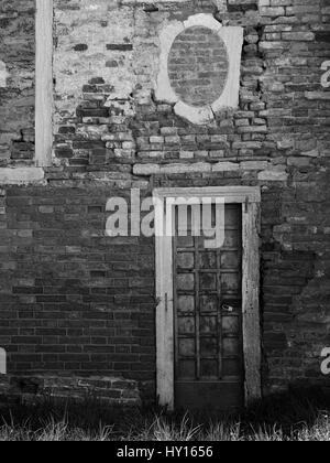 Old wooden paneled door with peeling paint and rusting hinges in an ancient brick wall Stock Photo