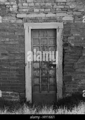 Old wooden paneled door with peeling paint and rusting hinges in an ancient brick wall Stock Photo